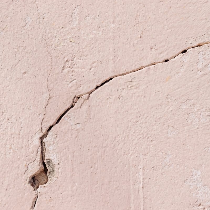 Close-up of crack on light pink plastered concrete wall